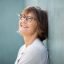 Close up side of smiling older woman with eyeglasses leaning against wall
